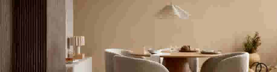 Minimalistische eetkamer met ronde houten tafel, beige stoelen, witte hanglamp en warme neutrale tinten.