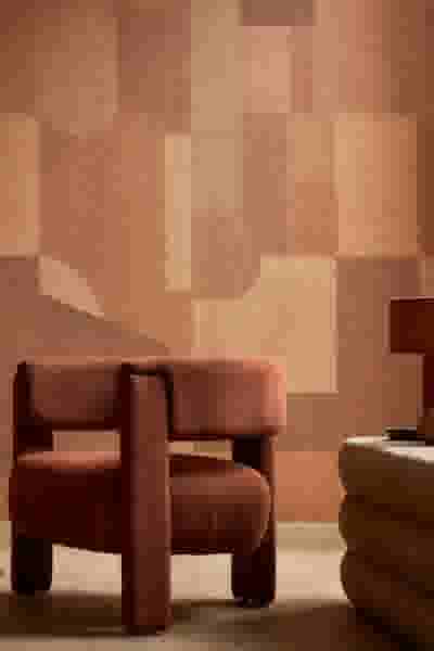 Terracotta fauteuil in een moderne woonkamer met geometrisch behang in warme aardetinten en een beige poef.