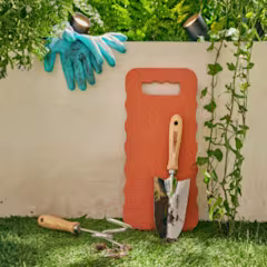 tuingereedschap zoals handschoenen, schepje, tuinkrabber en kniekussen tegen een muur in een tuin