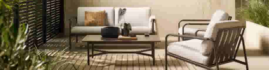 Modern terrasinterieur met witte bank, fauteuil, houten salontafel en decoratieve planten in een warme, natuurlijke sfeer.