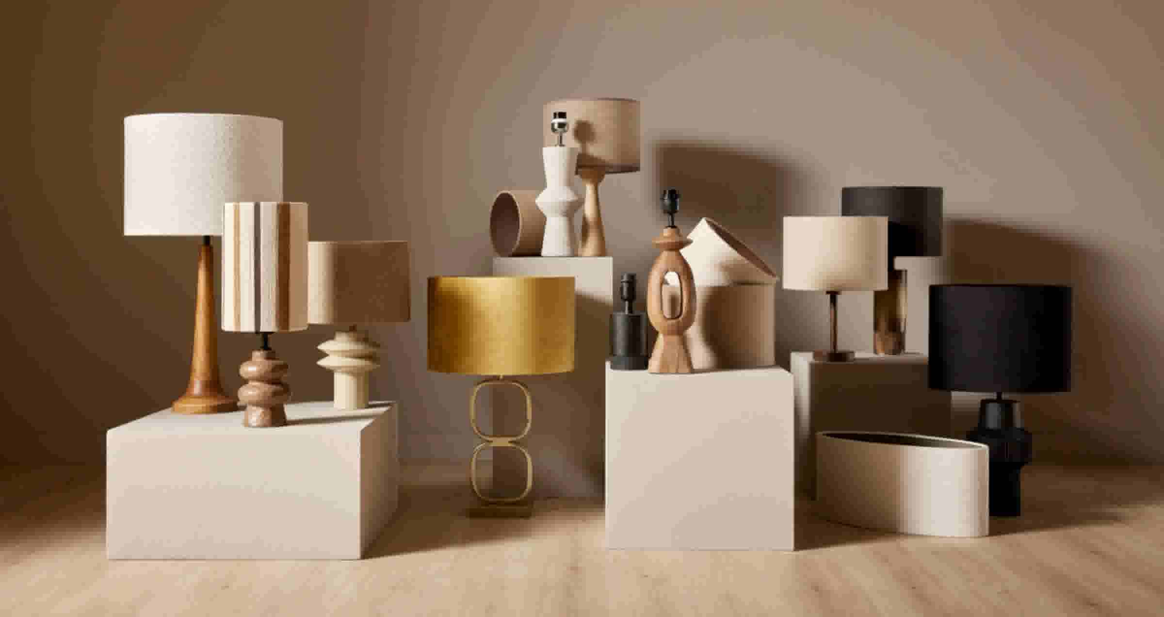 Diverse collectie designlampen in neutrale tinten, gerangschikt op witte sokkels tegen een beige achtergrond.