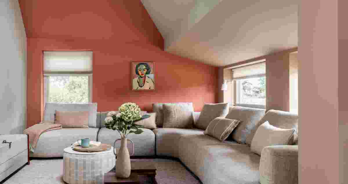 Moderne woonkamer met terracotta muur, grijze hoekbank, gestreepte poef en kunstwerk onder schuin plafond met ramen.