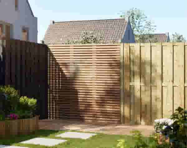 Houten tuinschermen in een tuin met terras, bloemen en stapstenen. Op de achtergrond zijn huizen zichtbaar onder een blauwe lucht.