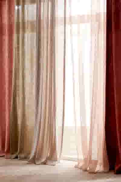 Lichtdoorlatende gordijnen in verschillende tinten roze en beige, die zacht gefilterd zonlicht binnenlaten door een raam.