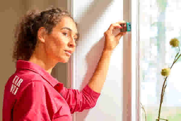 Karwei Specialist in roze shirt plaatst een meetapparaat op een raamkozijn