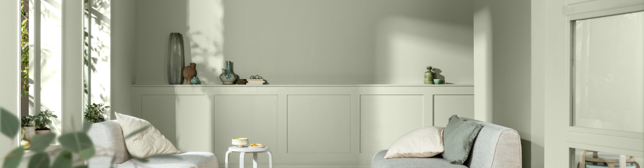 Lichte woonkamer met saliegroen geschilderde muren, twee grijze fauteuils, decoratieve vazen op planken en zonlicht.