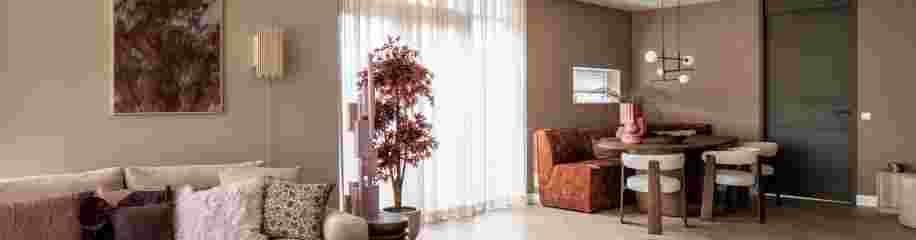 Moderne woonkamer met beige bank, bruine accenten, ronde eettafel en decoratieve rode plant bij het raam.