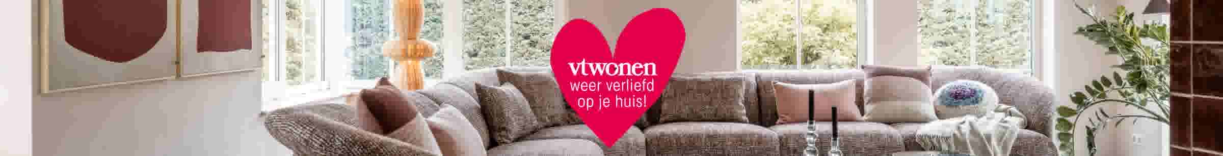 Moderne woonkamer met beige banken en groot roze hart met tekst 'vtwonen weer verliefd op je huis!'