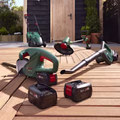 Accu gereedschap zoals heggenschaar, bladblazer, grasmaaier en bosmaaier van Bosch op een vlonder in de tuin, inclusief losse accu's