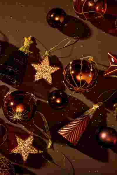 Feestelijke kerstdecoraties op donkere achtergrond: glanzende bruine ballen, gouden sterren en kleine kerstboompjes.