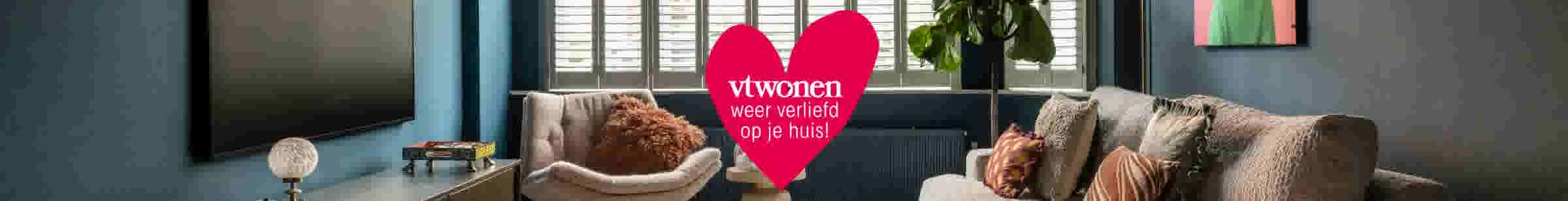 Moderne woonkamer met blauwe muur, beige bank en groot rood hart met tekst 'vtwonen weer verliefd op je huis!'