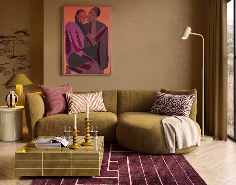 Woonkamer met mosterdgele bank, abstract kunstwerk aan beige muur, gouden salontafel en bordeauxrood tapijt.
