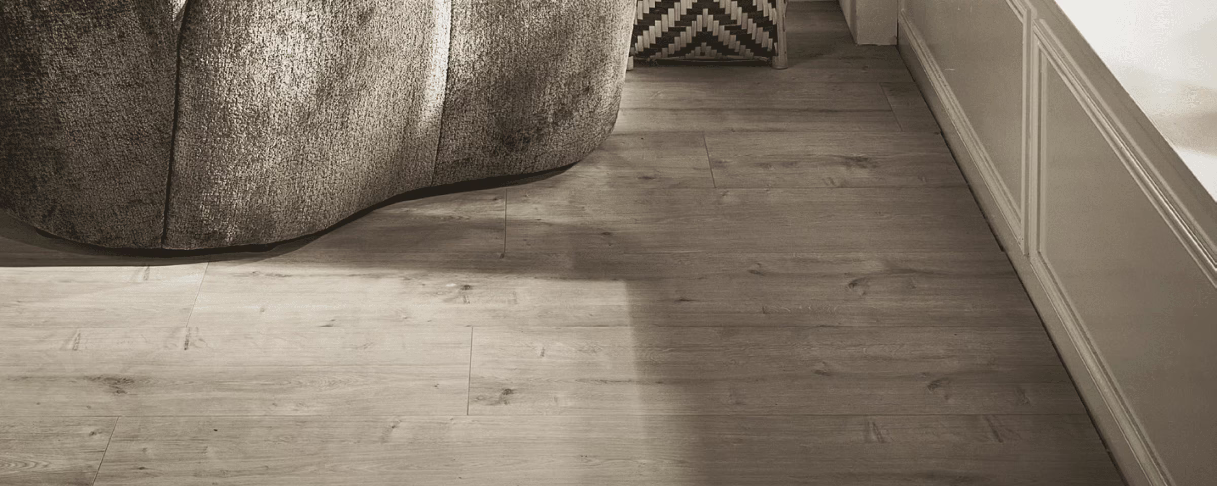 Lichte houten vloer met grijze bank en geometrisch tapijt in moderne woonkamer met witte lambrisering.