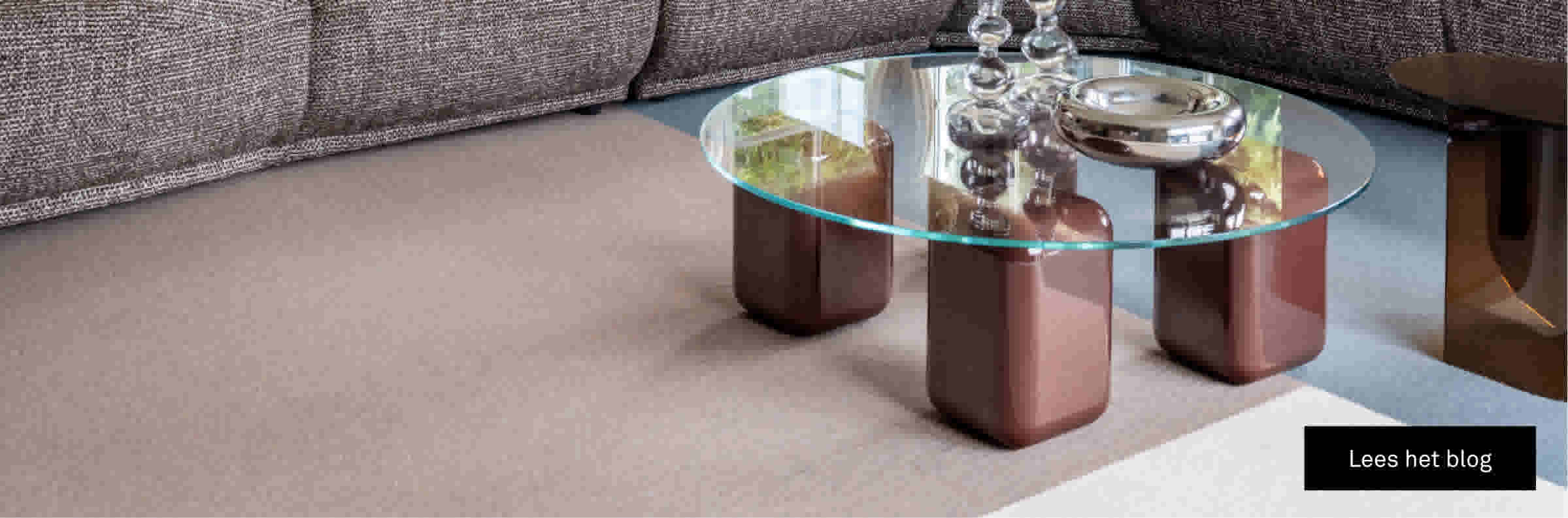 Salontafel op vloerbedekking in drie kleuren, op de achtergrond zie je een bank. Op het beeld staat een button naar lees het blog. 