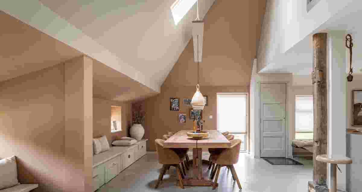 Moderne eetkamer met houten tafel, roze stoelen, hoog plafond en warme aardtinten in open ruimte met natuurlijk licht.