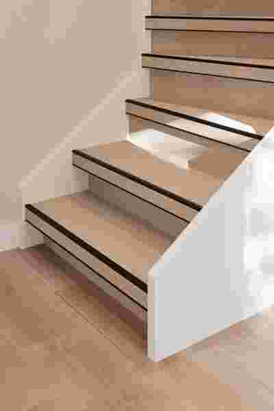 Houten trap met lichte eiken treden en zwarte antislipstrips, witte stootborden en lichte houten vloer eronder.