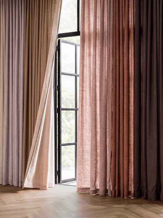 Meerkleurige gordijnen in beige, roze en bruin tinten bij een open zwart metalen raam met uitzicht op groen.