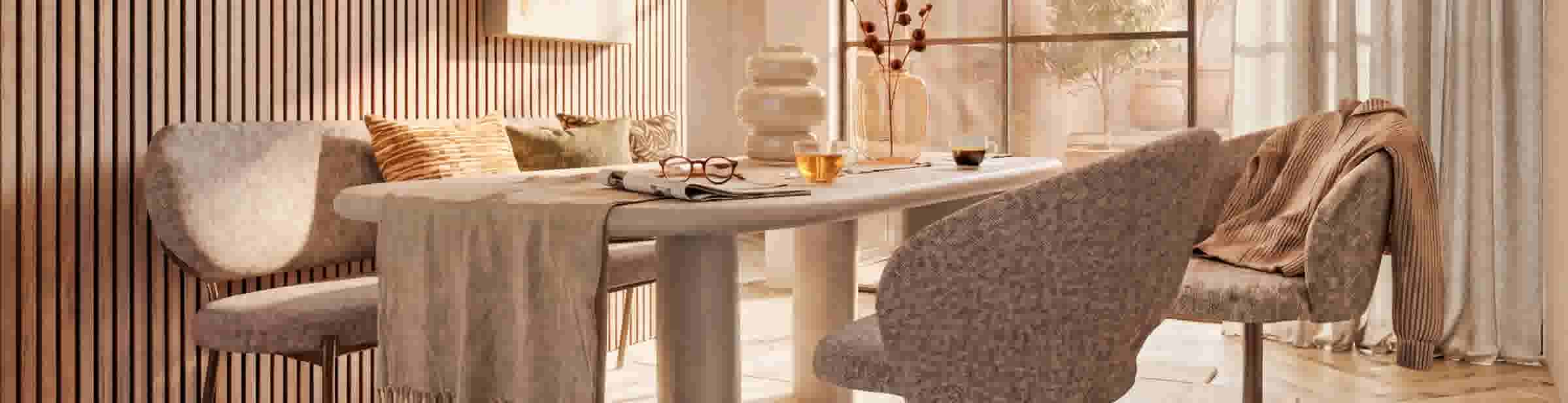 Sfeerbeeld van een eethoek met een houten lamellenwand, bank en stoelen met kussens en plaid, tafel gedekt met thee, koffie, bril en tijdschrift, vazen en planten bij een raam met vitrage.