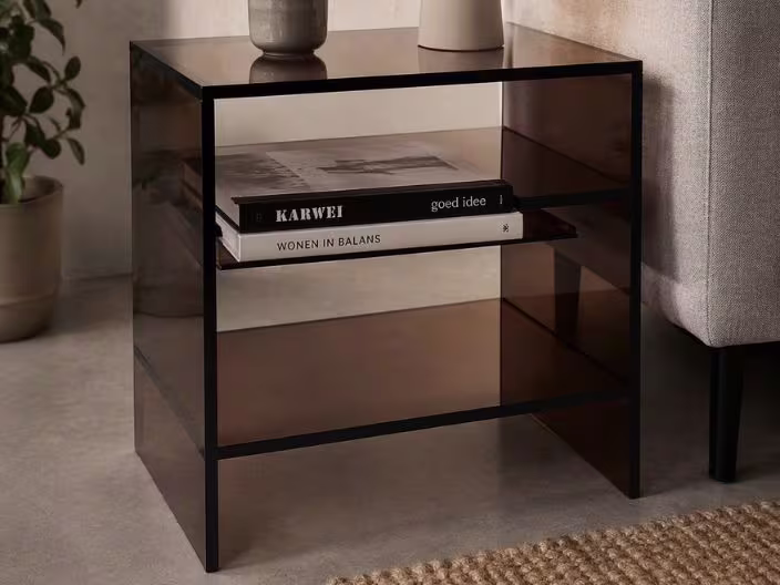 Zwart bijzettafeltje met rookglas kunststof, boeken op het schap en een vaas bovenop, naast een bank in een woonkamer.