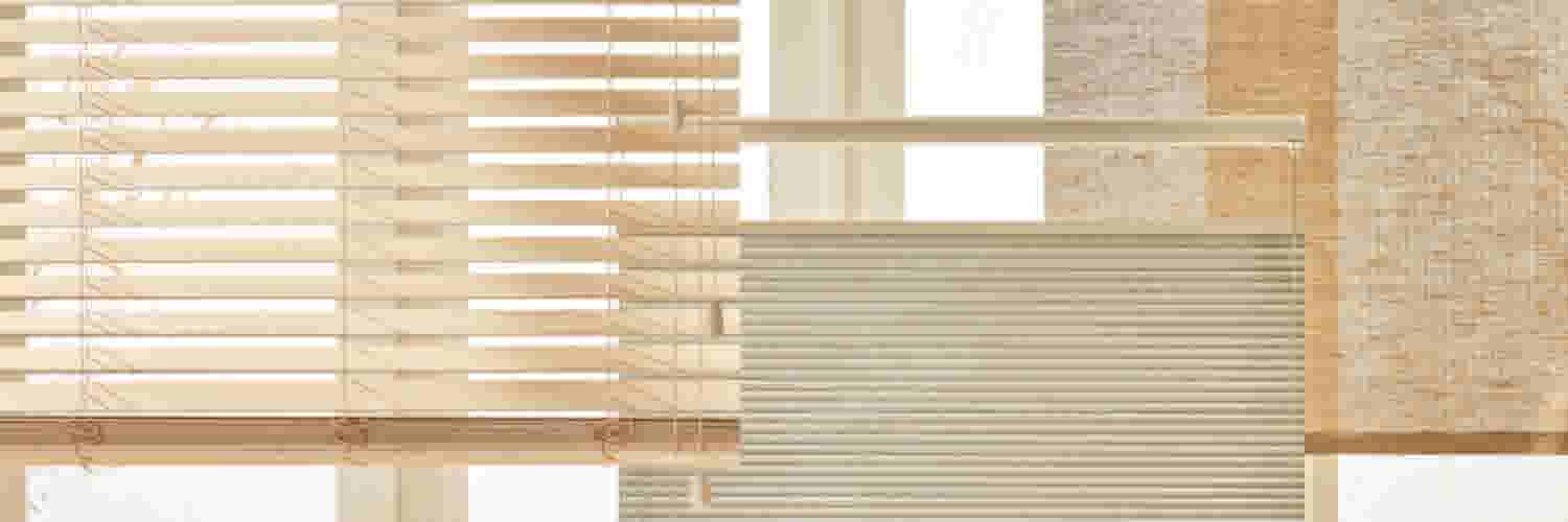 Verschillende soorten raamdecoratie, waaronder houten jaloezieën, plisségordijnen en geweven rolgordijnen, in een lichte, moderne woonkamer.