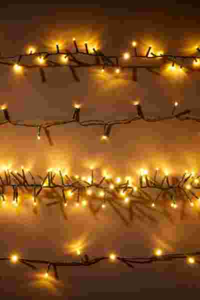 Rijen warme gele kerstlichtjes op draden tegen een neutrale achtergrond, creëren een gezellige feestelijke sfeer.