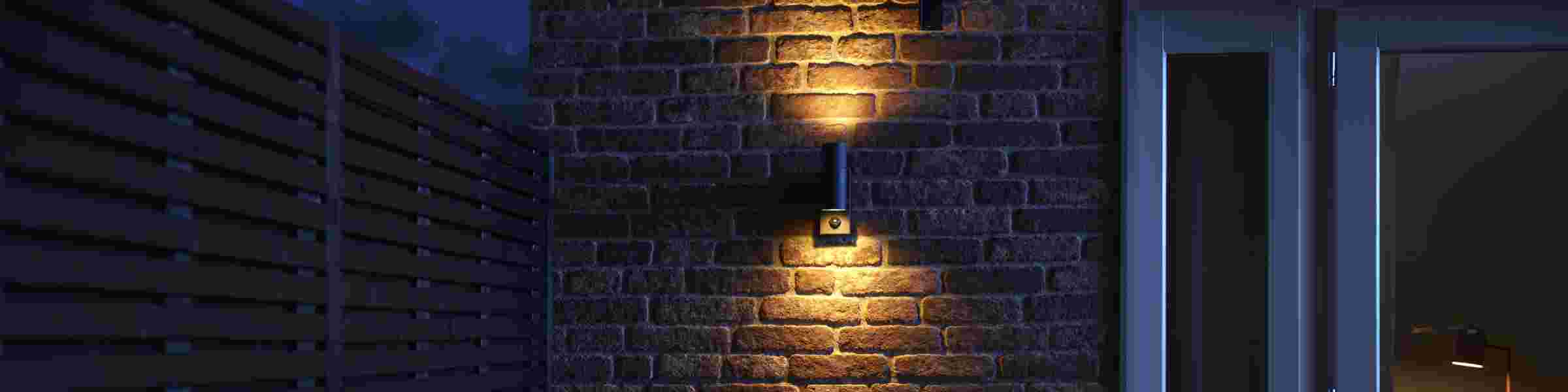Moderne wandlamp verlicht een bakstenen muur met warm geel licht in een donkere ruimte met blauwe tinten.