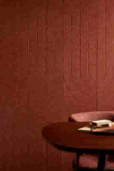 Terracotta wandpaneel met geometrisch patroon en een houten tafel met enkele items erop in de voorgrond.