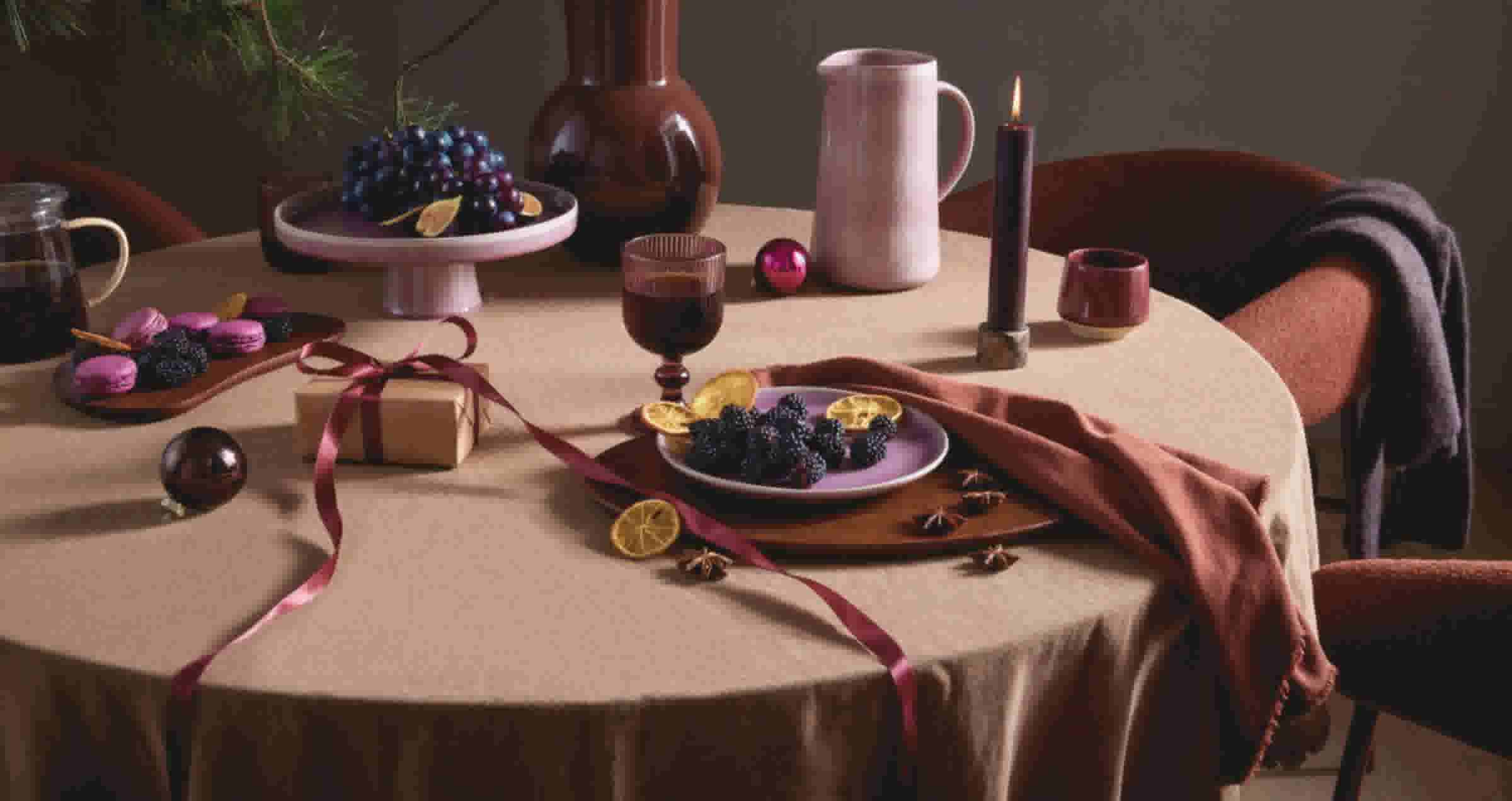 Feestelijke tafel met bramen, druiven, macarons, een cadeautje met roze lint, kaars en servies in warme herfsttinten.
