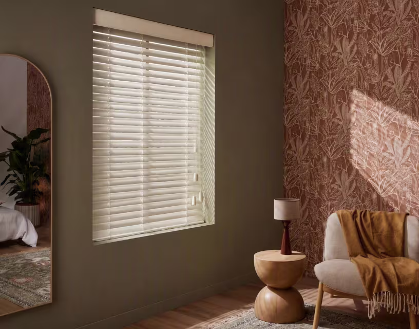 Moderne slaapkamer met olijfgroene muren, witte jaloezieën, botanisch behang in terracotta en beige fauteuil met okergele plaid.