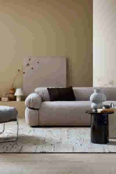 Moderne woonkamer met beige bank, zwarte bijzettafel en decoratieve vazen tegen een warme gele muur.