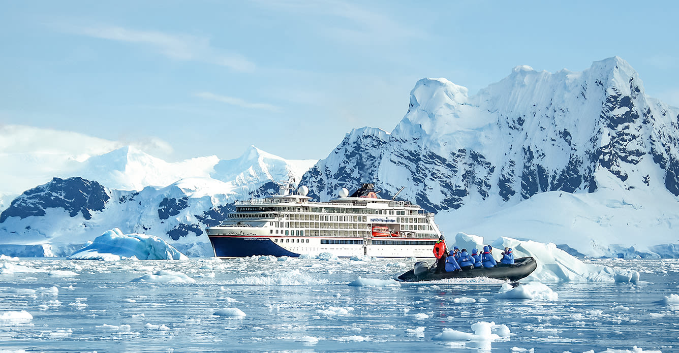 Expeditionsschiff vor einem Eisberg mit Menschen in einem Schlauchboot im Vordergrund