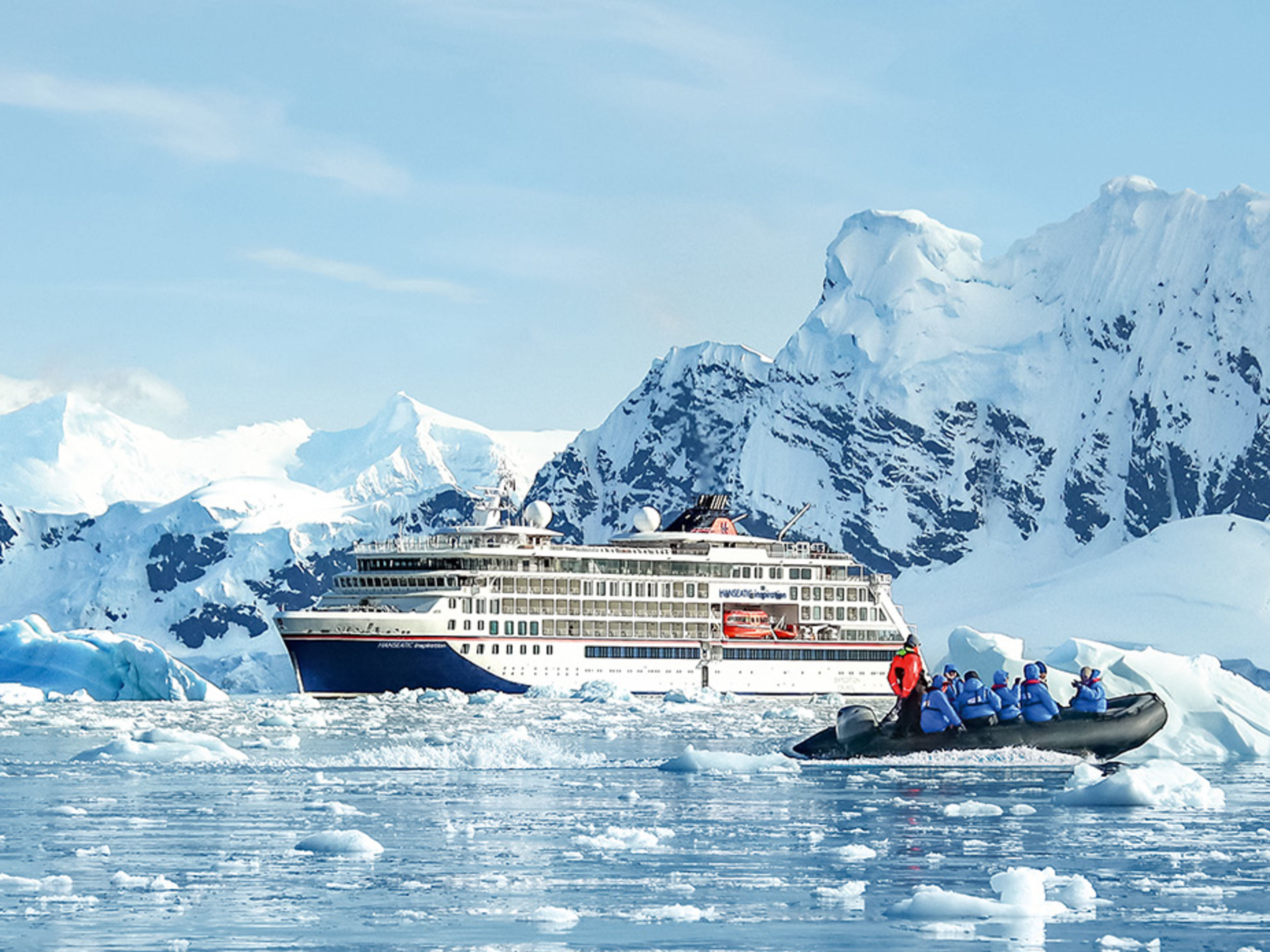 Expeditionsschiff vor einem Eisberg mit Menschen in einem Schlauchboot im Vordergrund