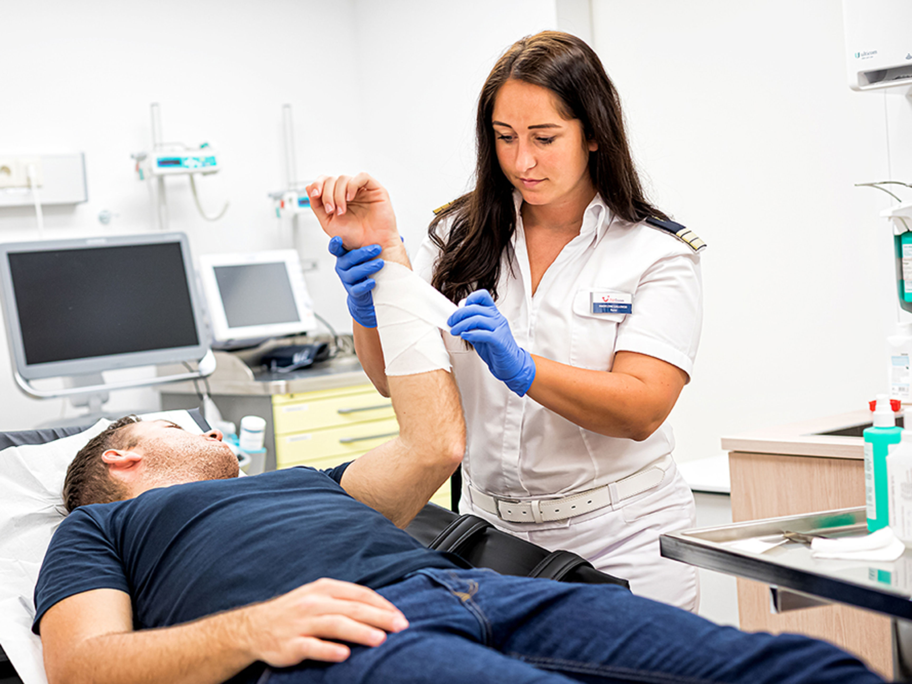 Im Behandlungszimmer. Die weibliche Nurse verbindet das Handgelenk eines männlichen Patienten, der auf einer Liege liegt.