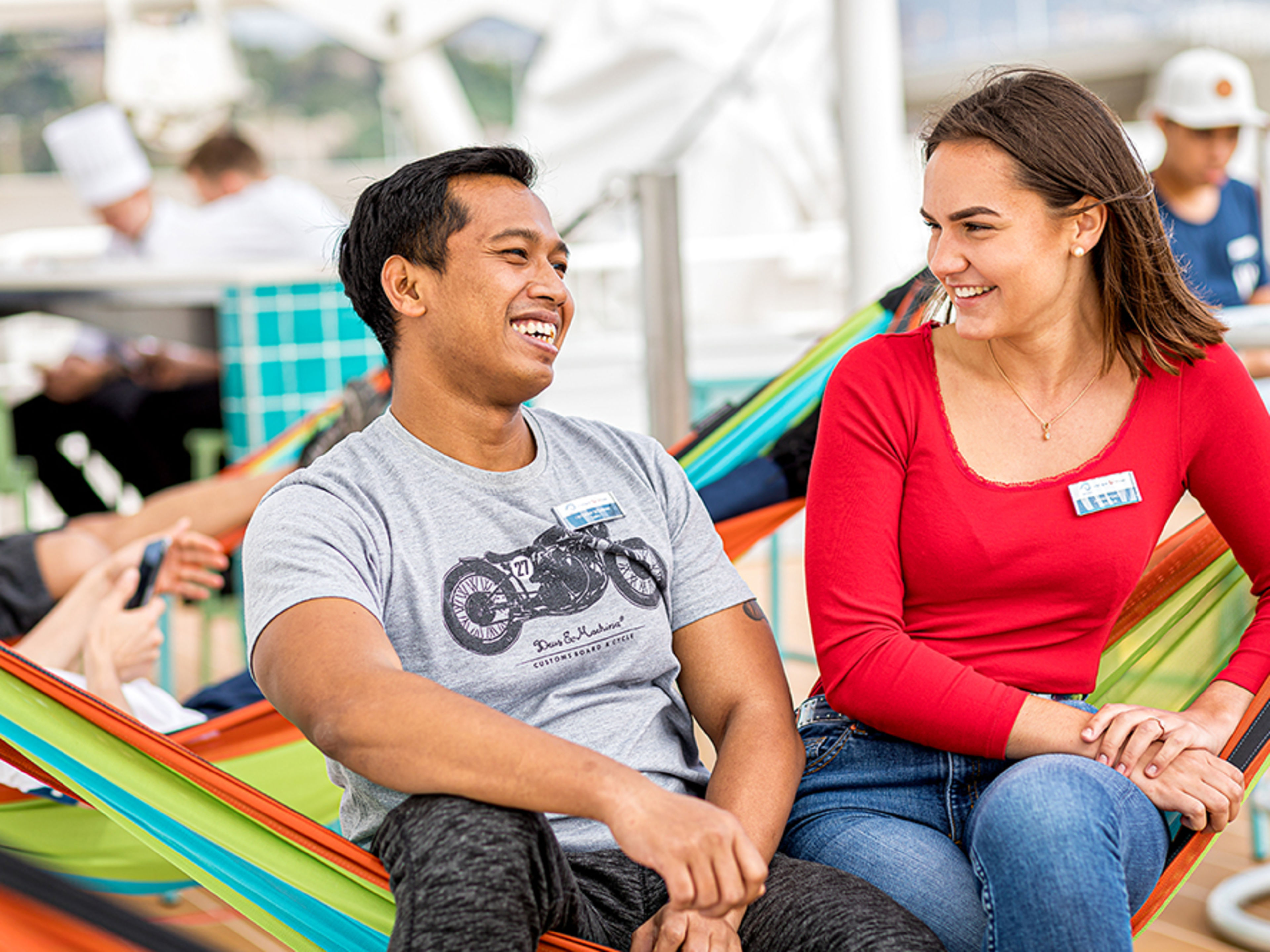 Crewdeck. Zwei Crew Member sitzen nebeneinander in einer bunten Hängematte und lächeln sich an.