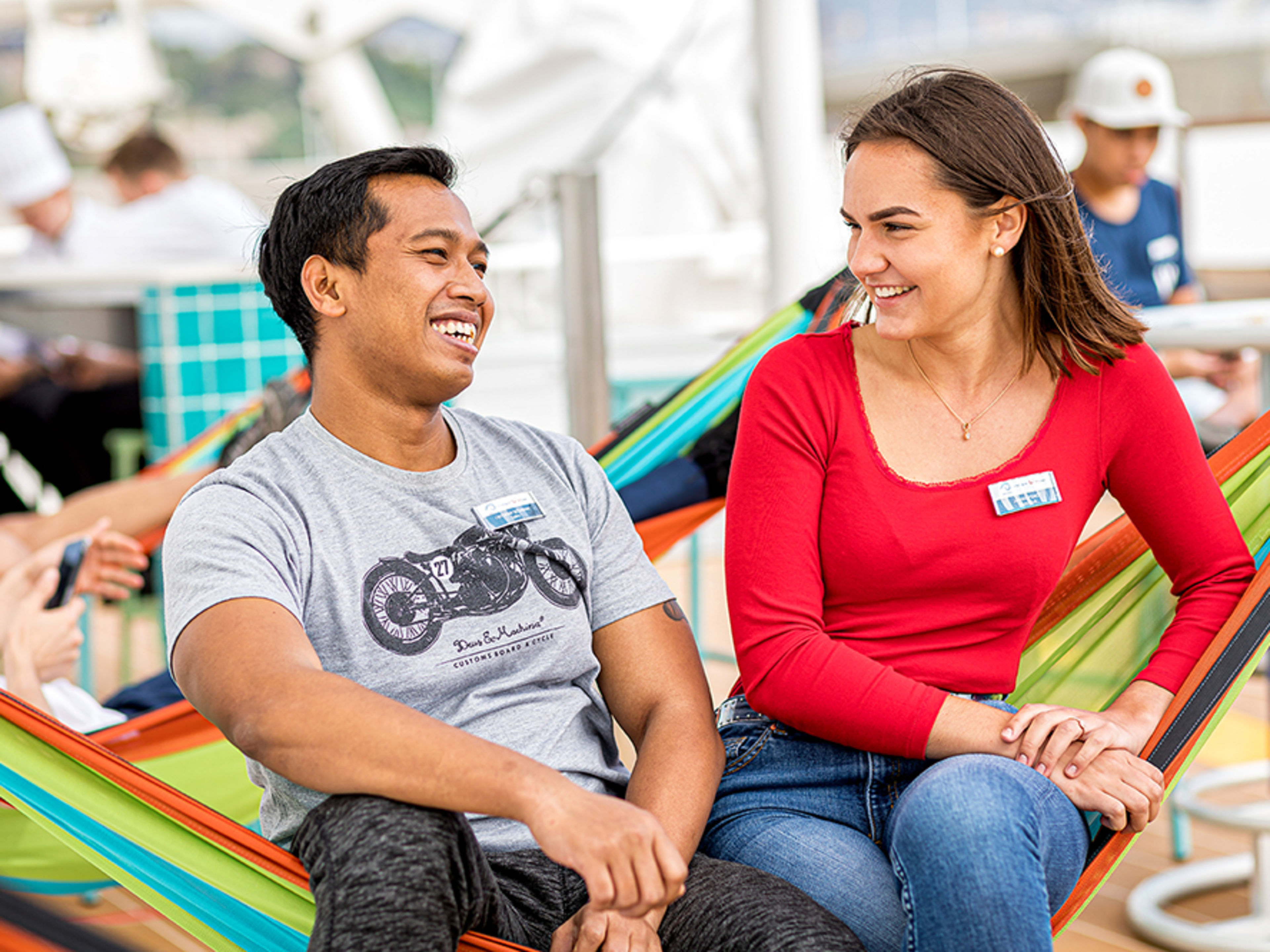 Crewdeck. Zwei Crew Member sitzen nebeneinander in einer bunten Hängematte und lächeln sich an.