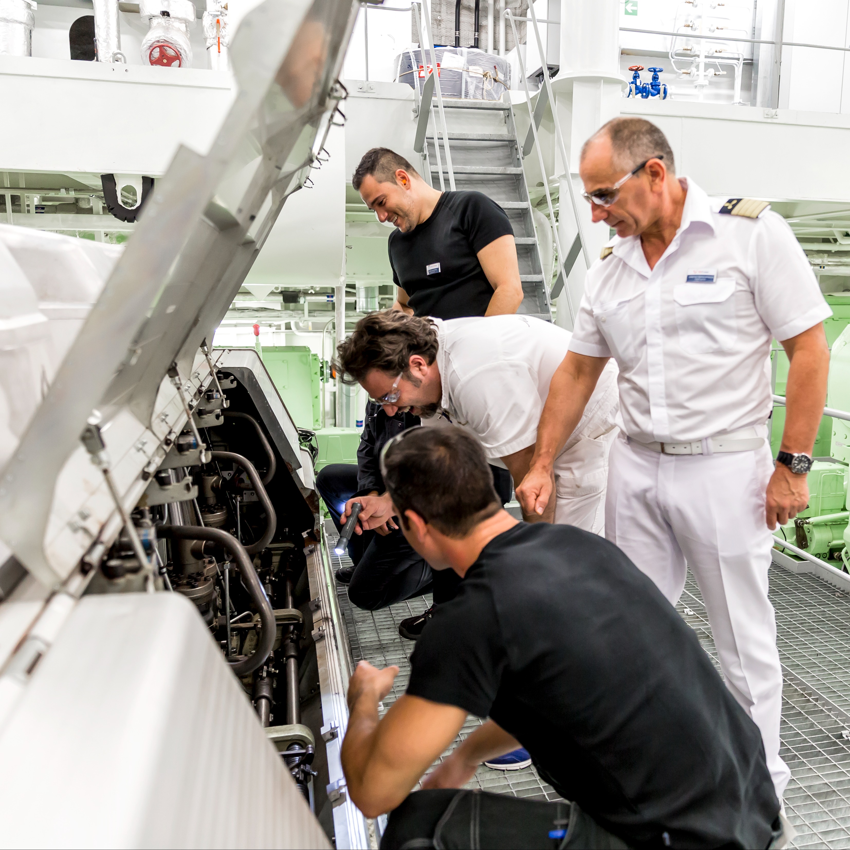 Maschinenraum eines Schiffes. Ein Team von vier männlichen Personen untersucht gemeinsam eine Maschine. 