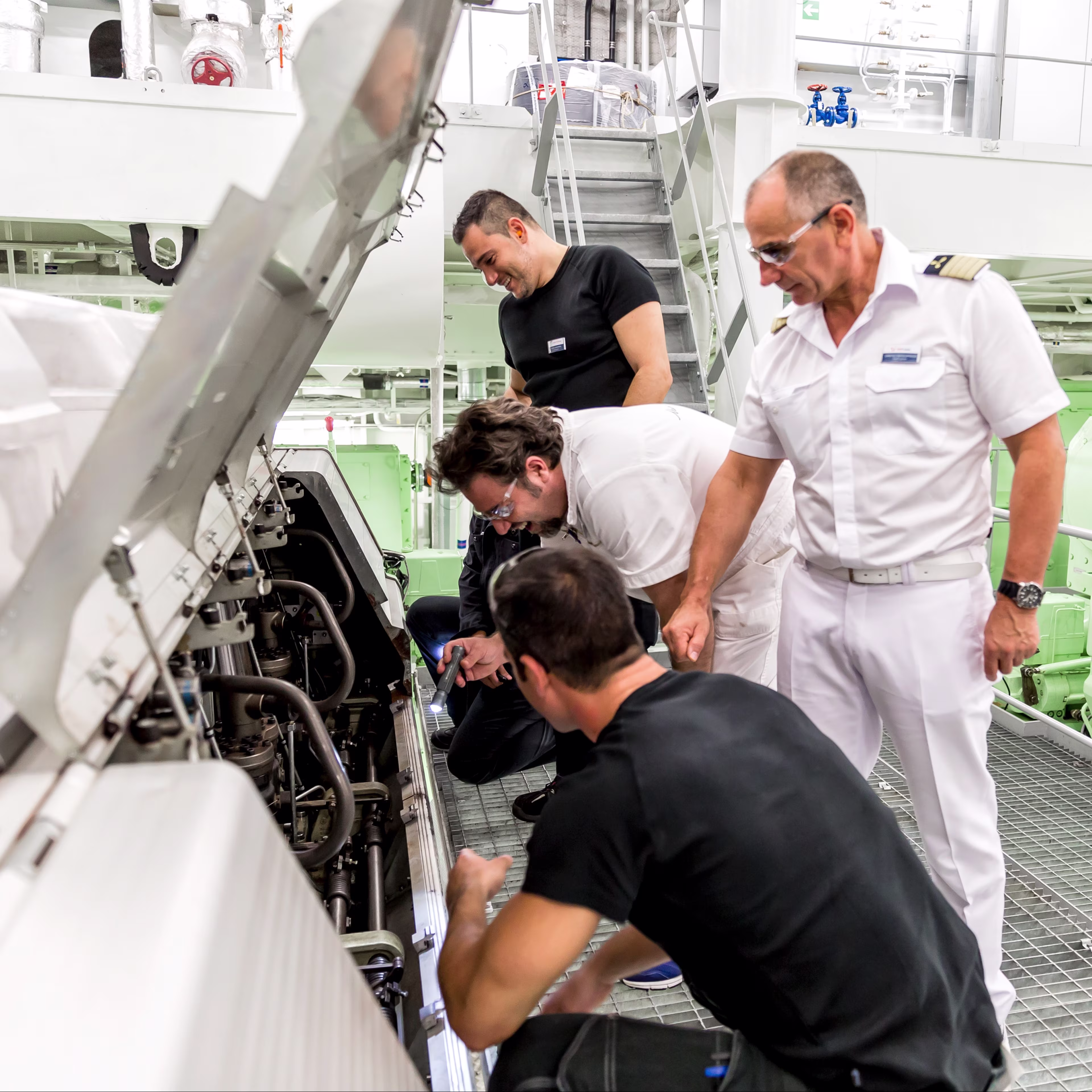 Maschinenraum eines Schiffes. Ein Team von vier männlichen Personen untersucht gemeinsam eine Maschine.