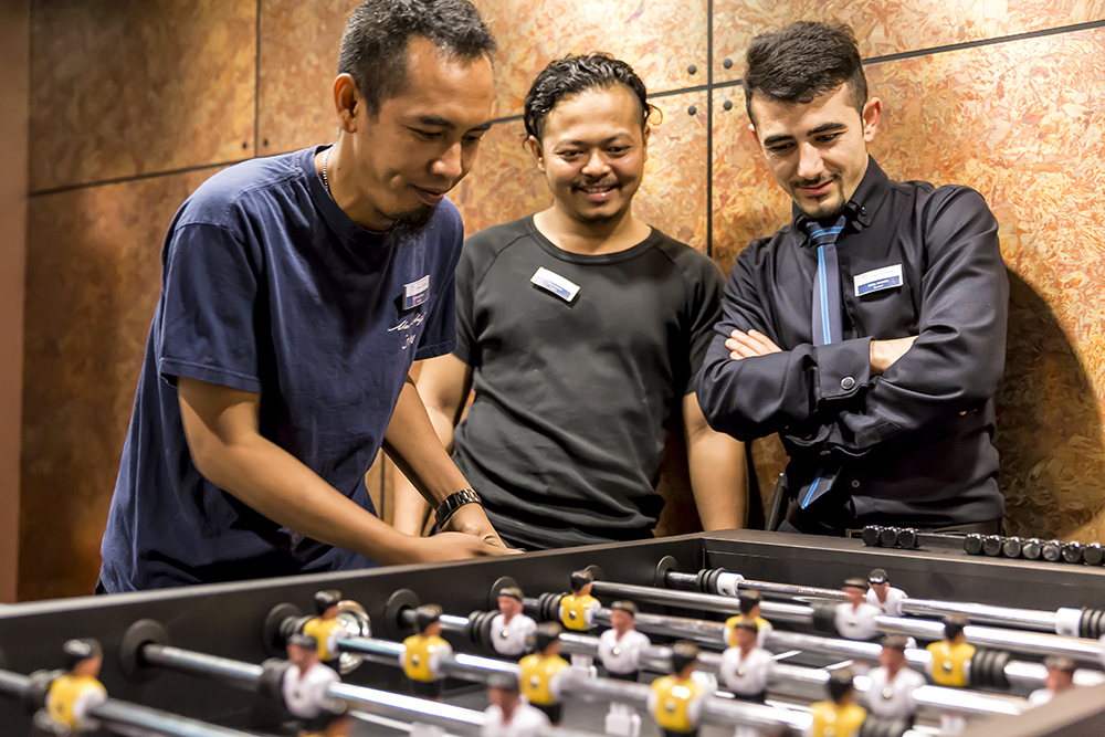 Drei männliche Crew Member spielen an einem Tischfußball-Kicker. 