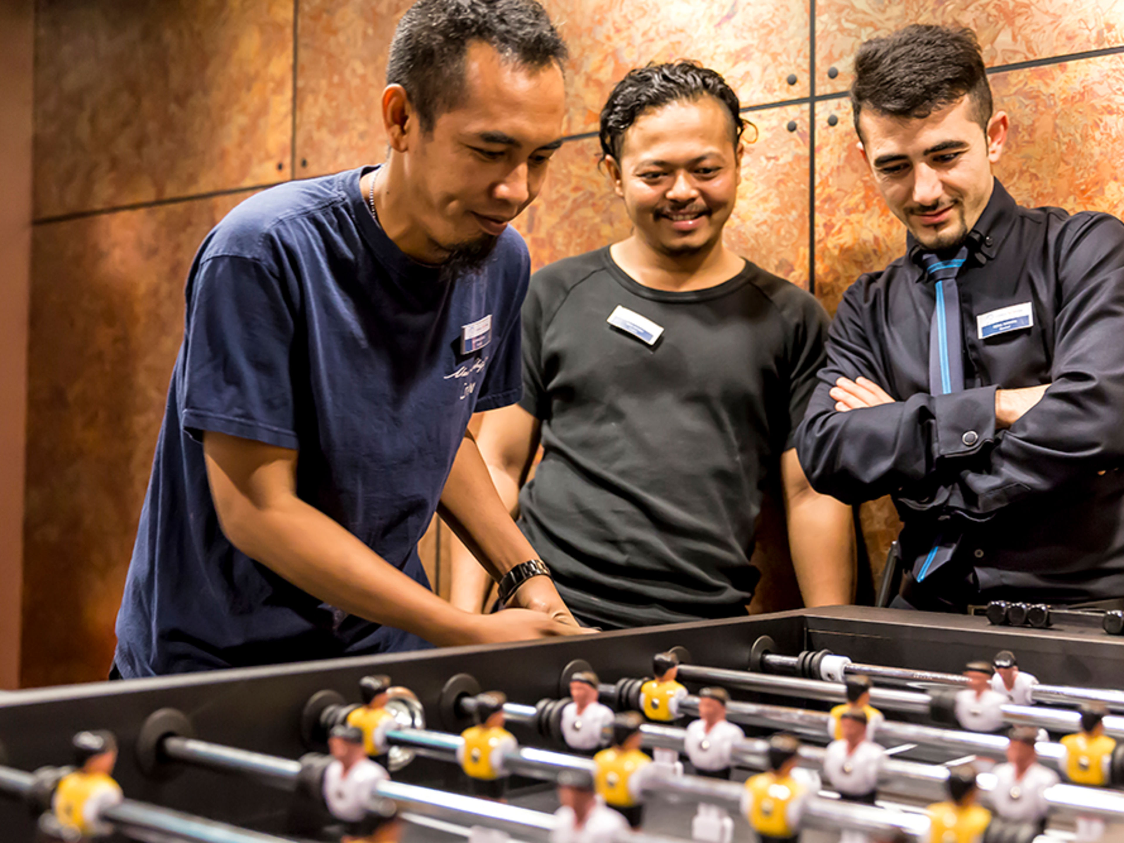 Drei männliche Crew Member spielen an einem Tischfußball-Kicker.
