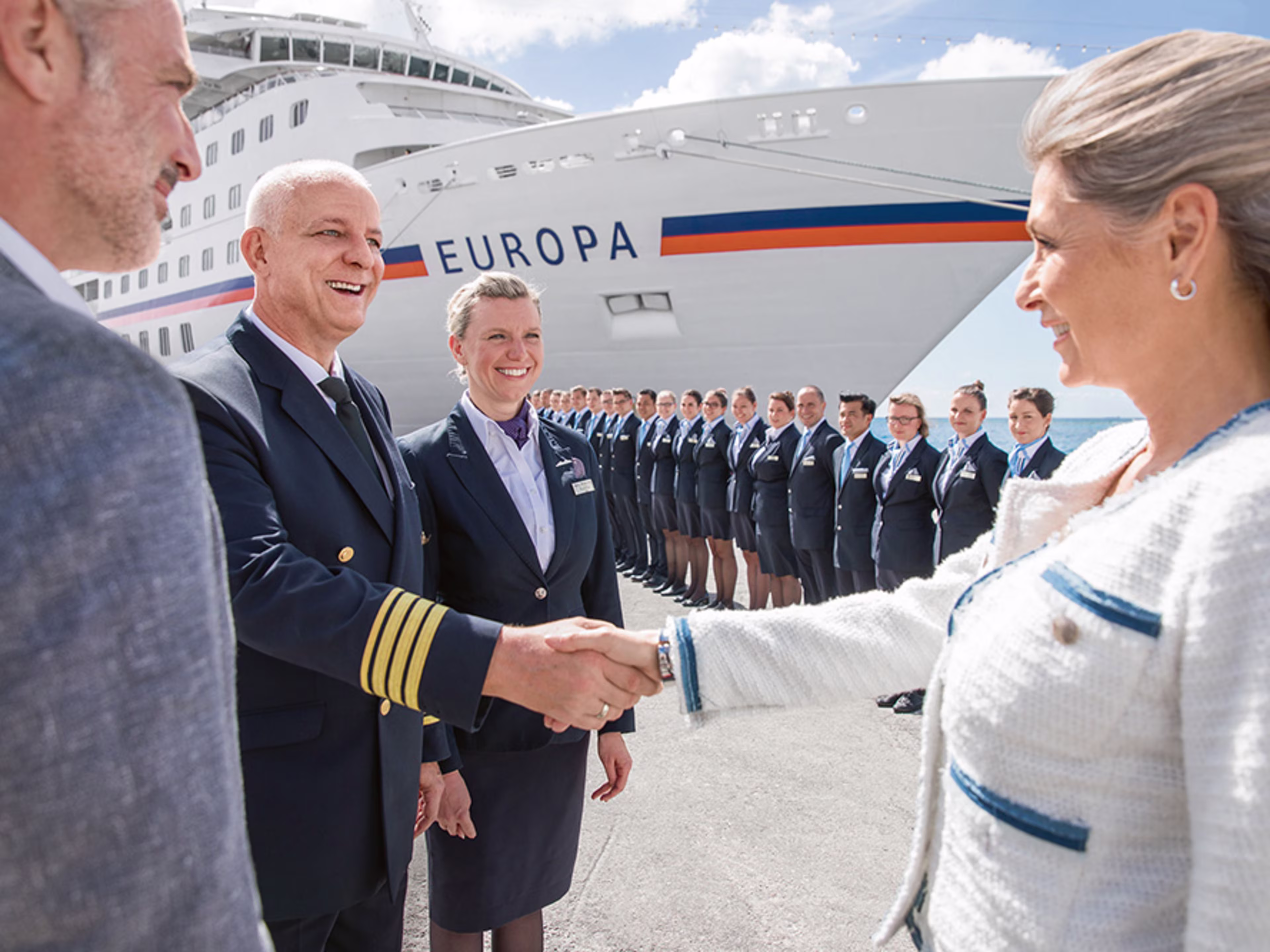 Spalier stehen vor der MS EUROPA. Davor gibt ein weiblicher Gast einem männlichen Offizier die Hand.