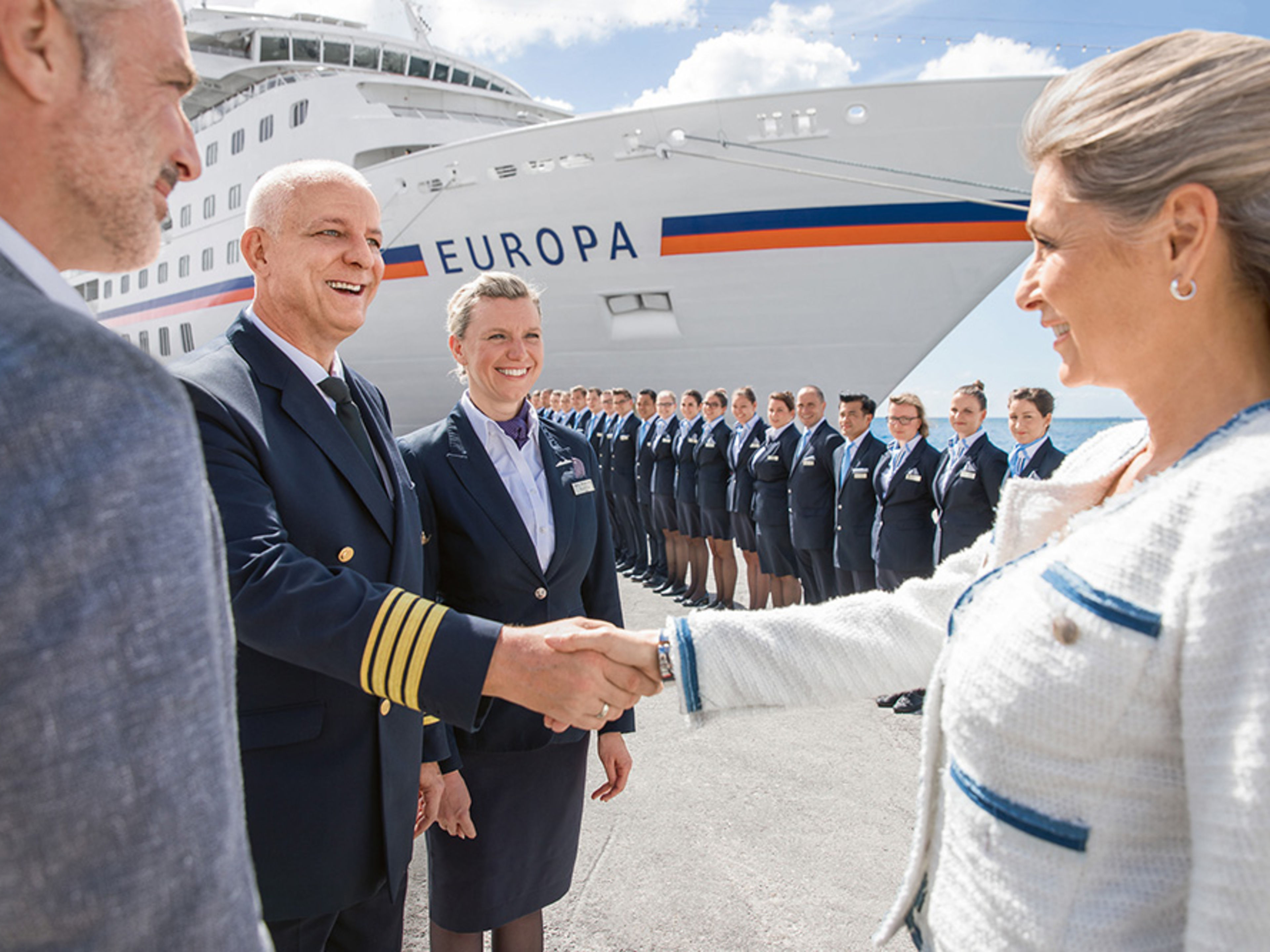 Spalier stehen vor der MS EUROPA. Davor gibt ein weiblicher Gast einem männlichen Offizier die Hand.