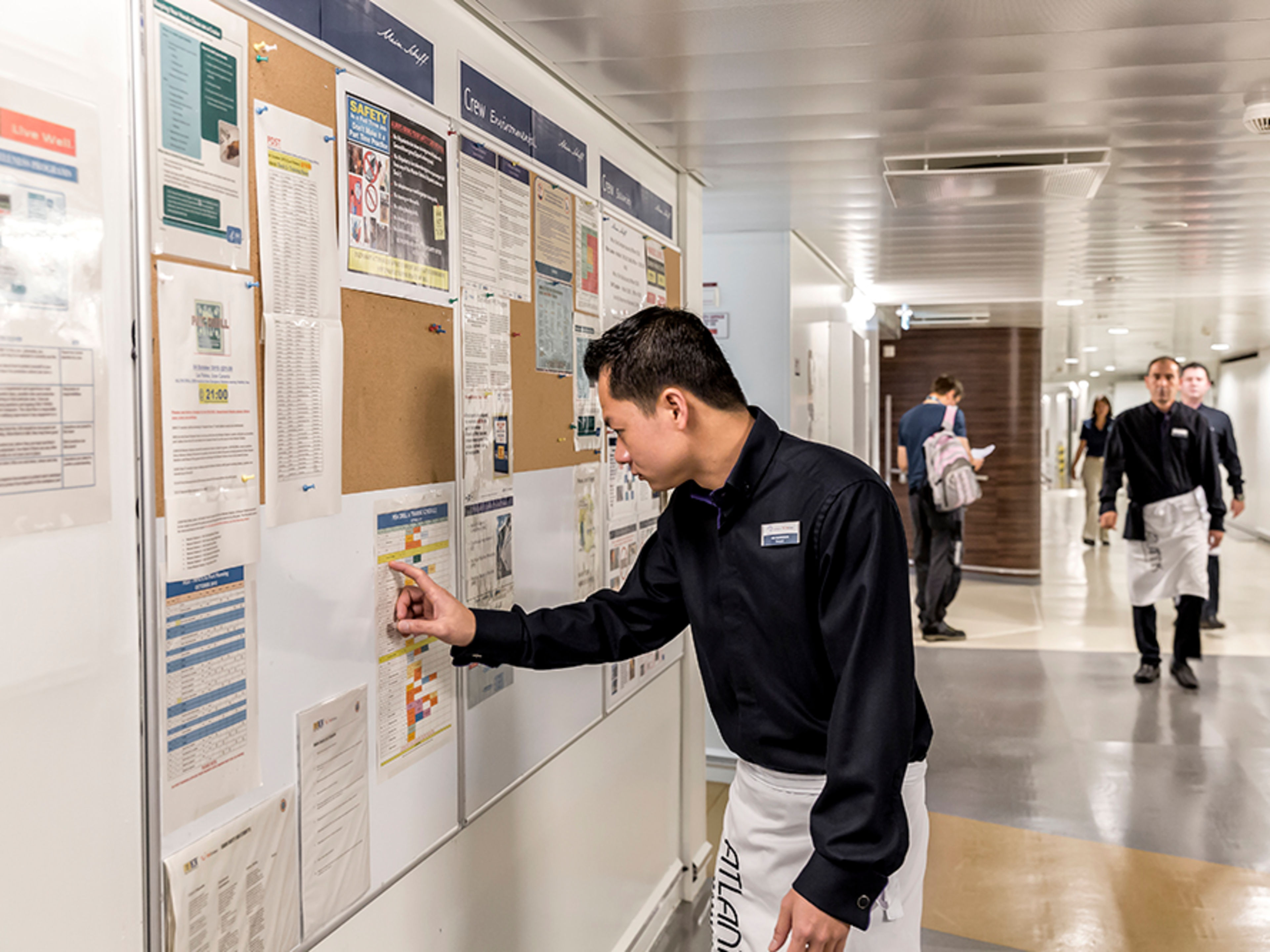 Beschäftigter Flur im Crew Bereich. Ein männliches Crew Member steht an einem Aushang und überprüft die Trainingszeiten.