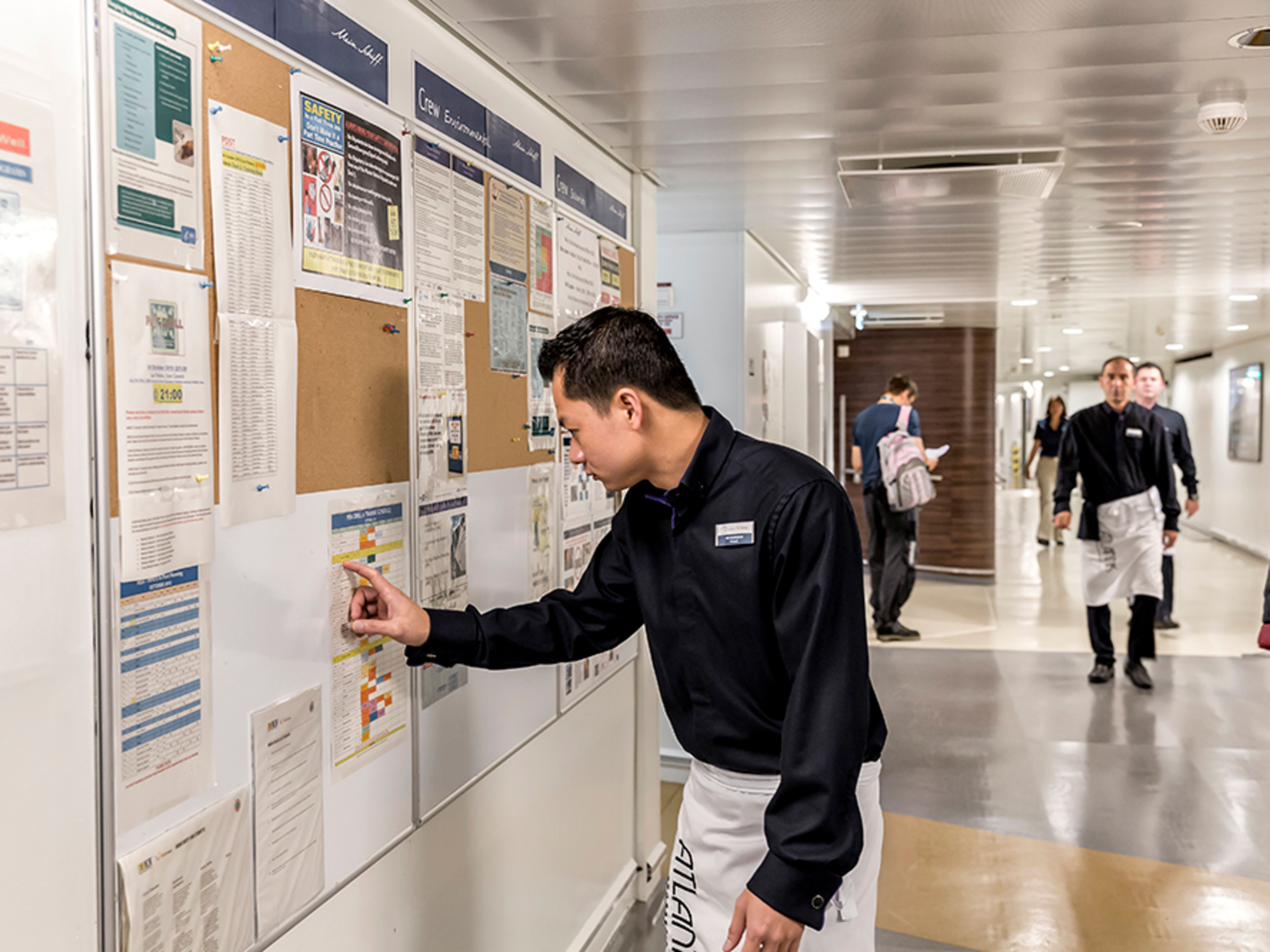 Beschäftigter Flur im Crew Bereich. Ein männliches Crew Member steht an einem Aushang und überprüft die Trainingszeiten.