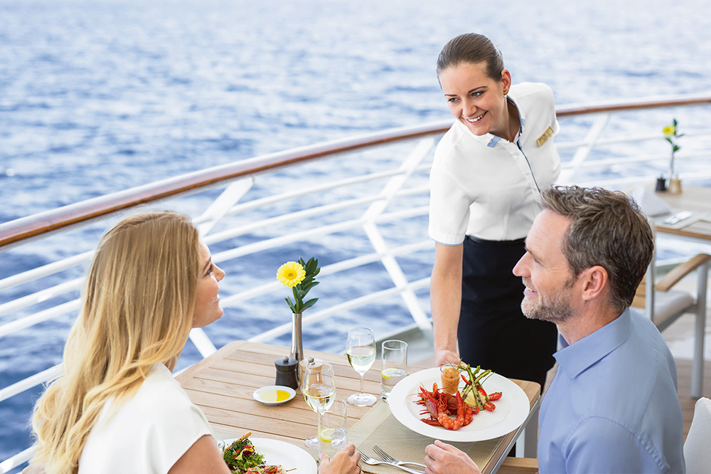 Restaurant auf dem Deck. Ein weibliches Crew Member serviert einem Pärchen das Essen. 