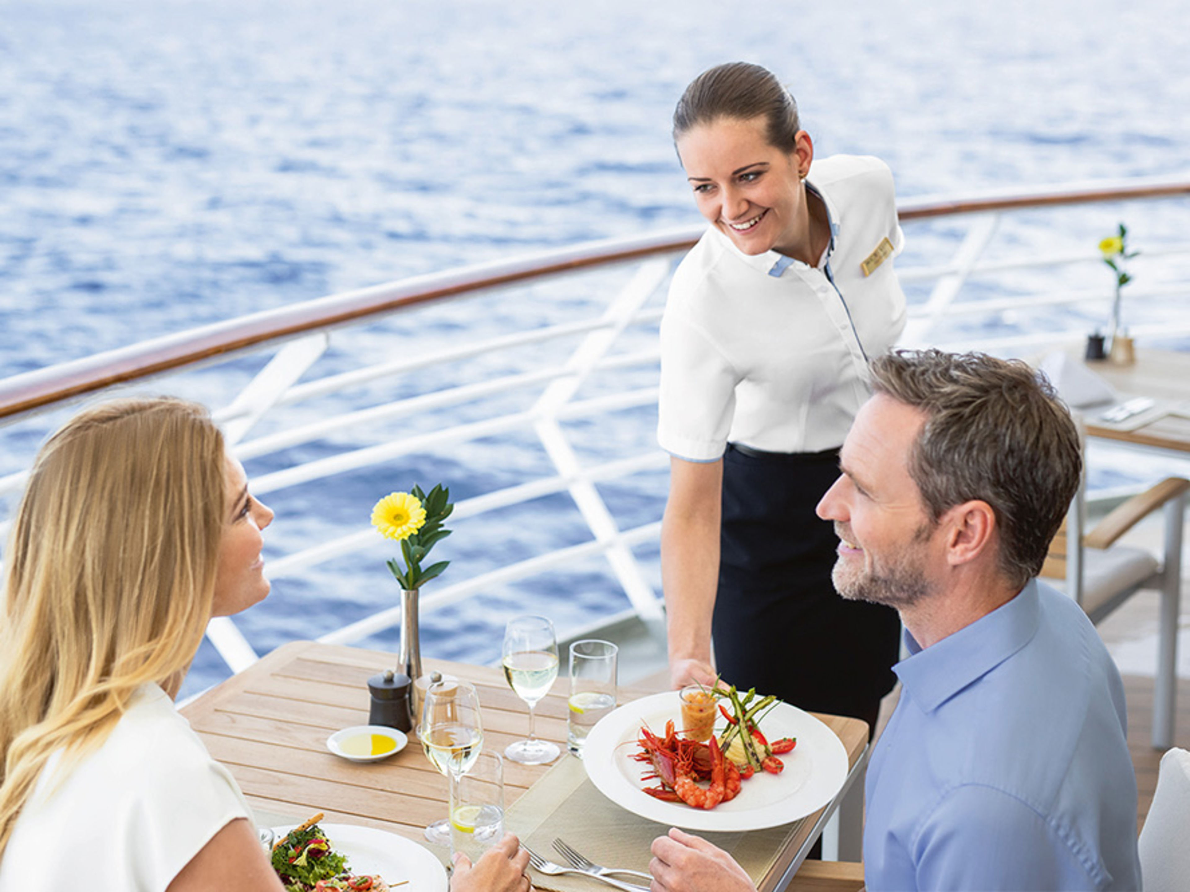 Restaurant auf dem Deck. Ein weibliches Crew Member serviert einem Pärchen das Essen.