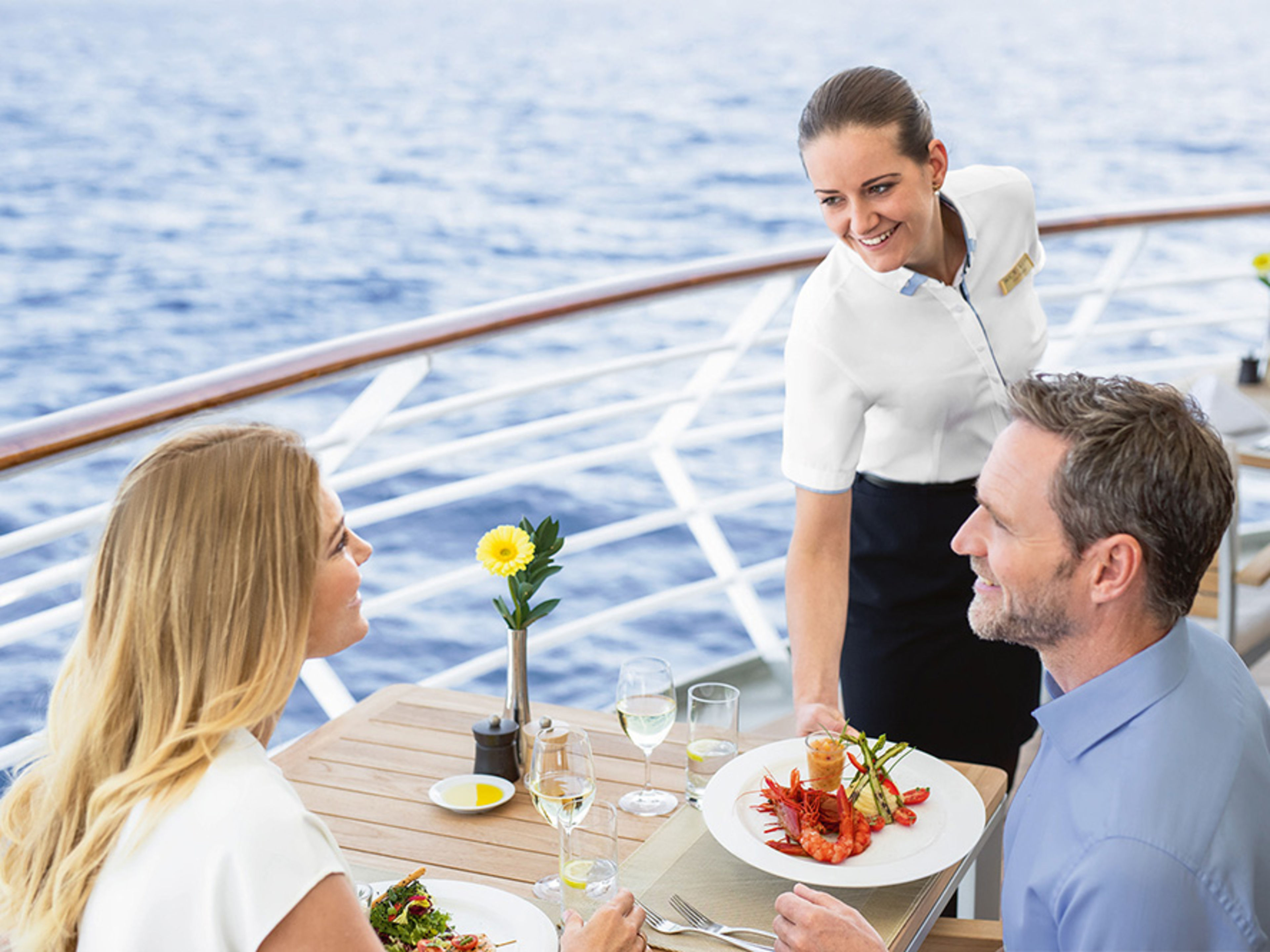 Restaurant auf dem Deck. Ein weibliches Crew Member serviert einem Pärchen das Essen.