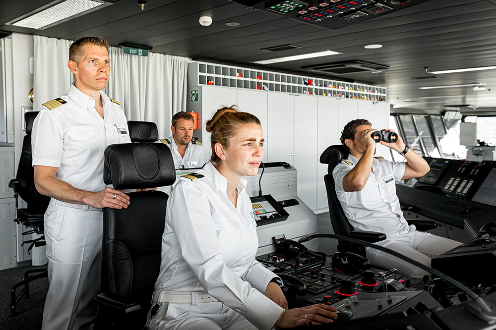 Schiffsbrücke. Drei Offiziere und der Kapitän halten Wache. Ein Offizier schaut durch ein professioneller Fernglas. 