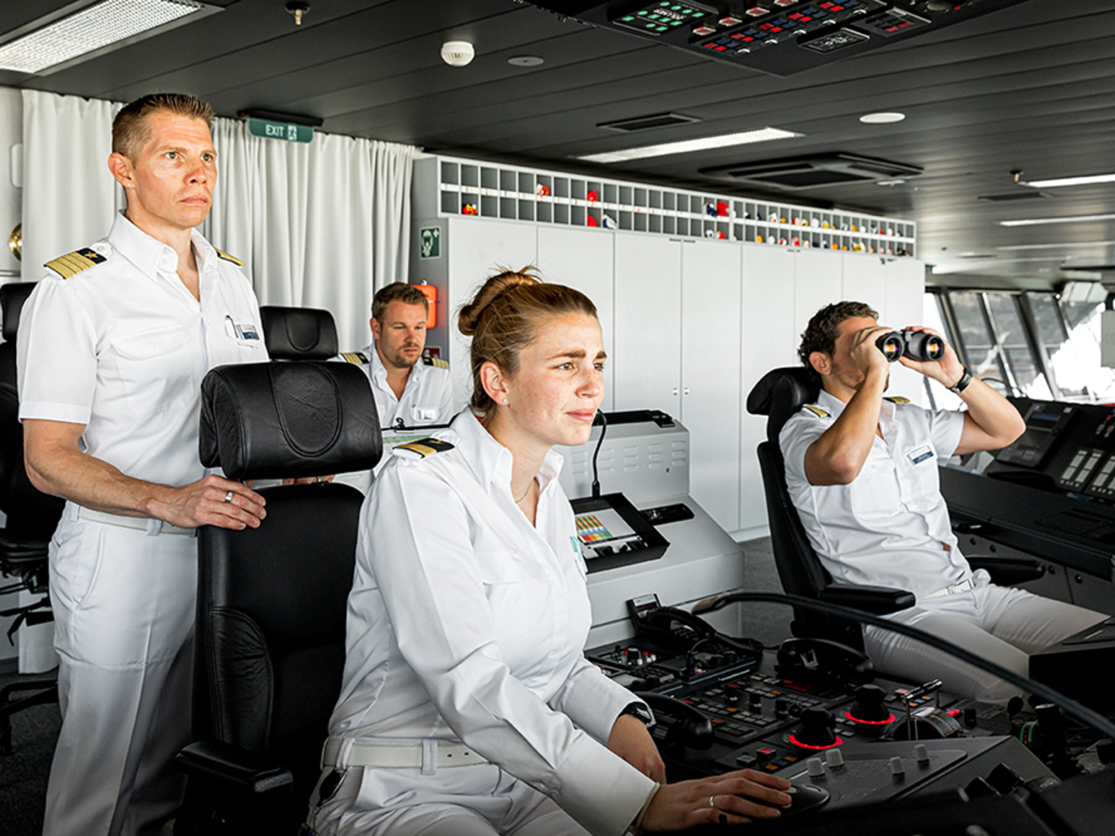 Schiffsbrücke. Drei Offiziere und der Kapitän halten Wache. Ein Offizier schaut durch ein professioneller Fernglas.