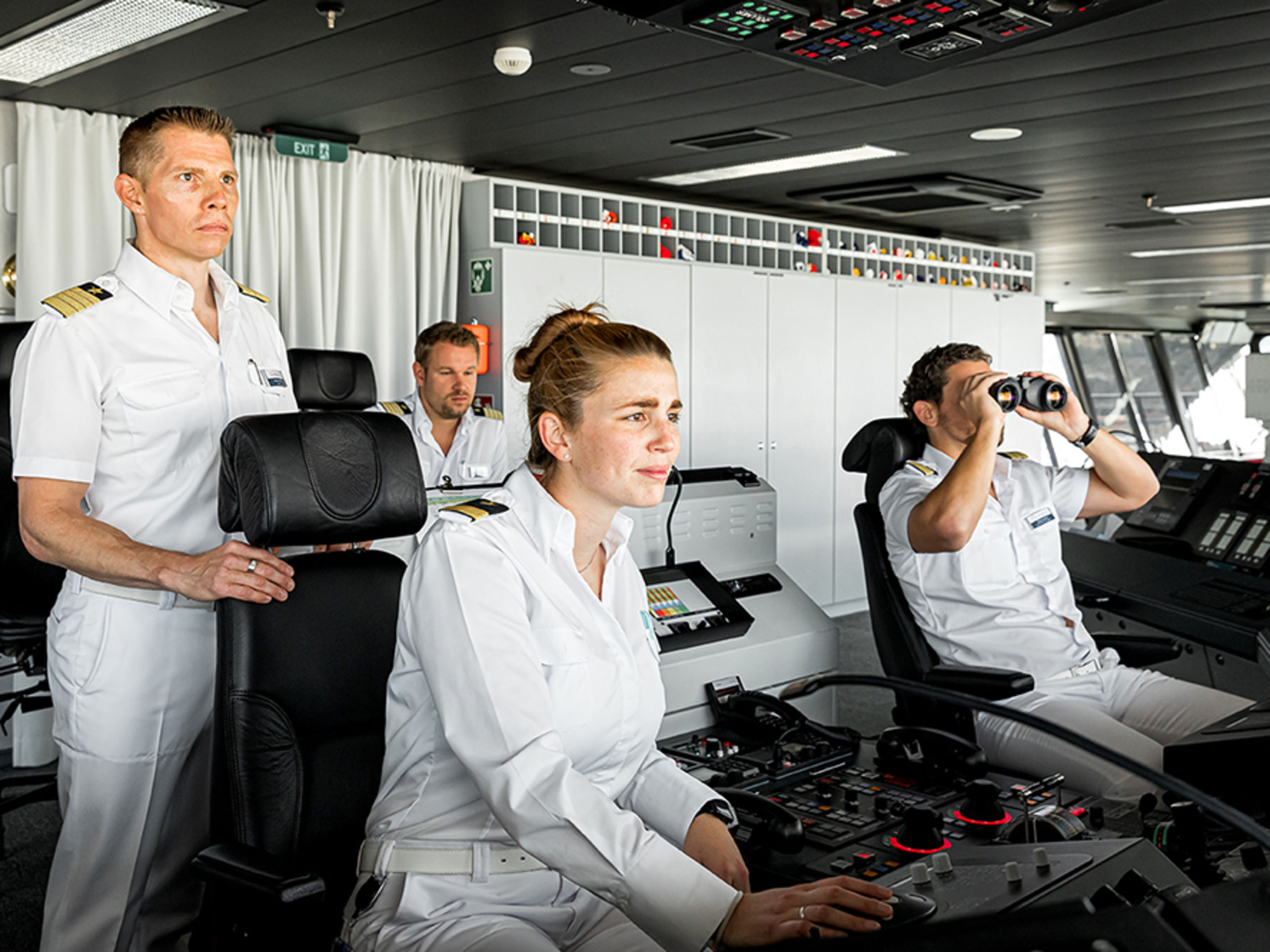 Schiffsbrücke. Drei Offiziere und der Kapitän halten Wache. Ein Offizier schaut durch ein professioneller Fernglas.