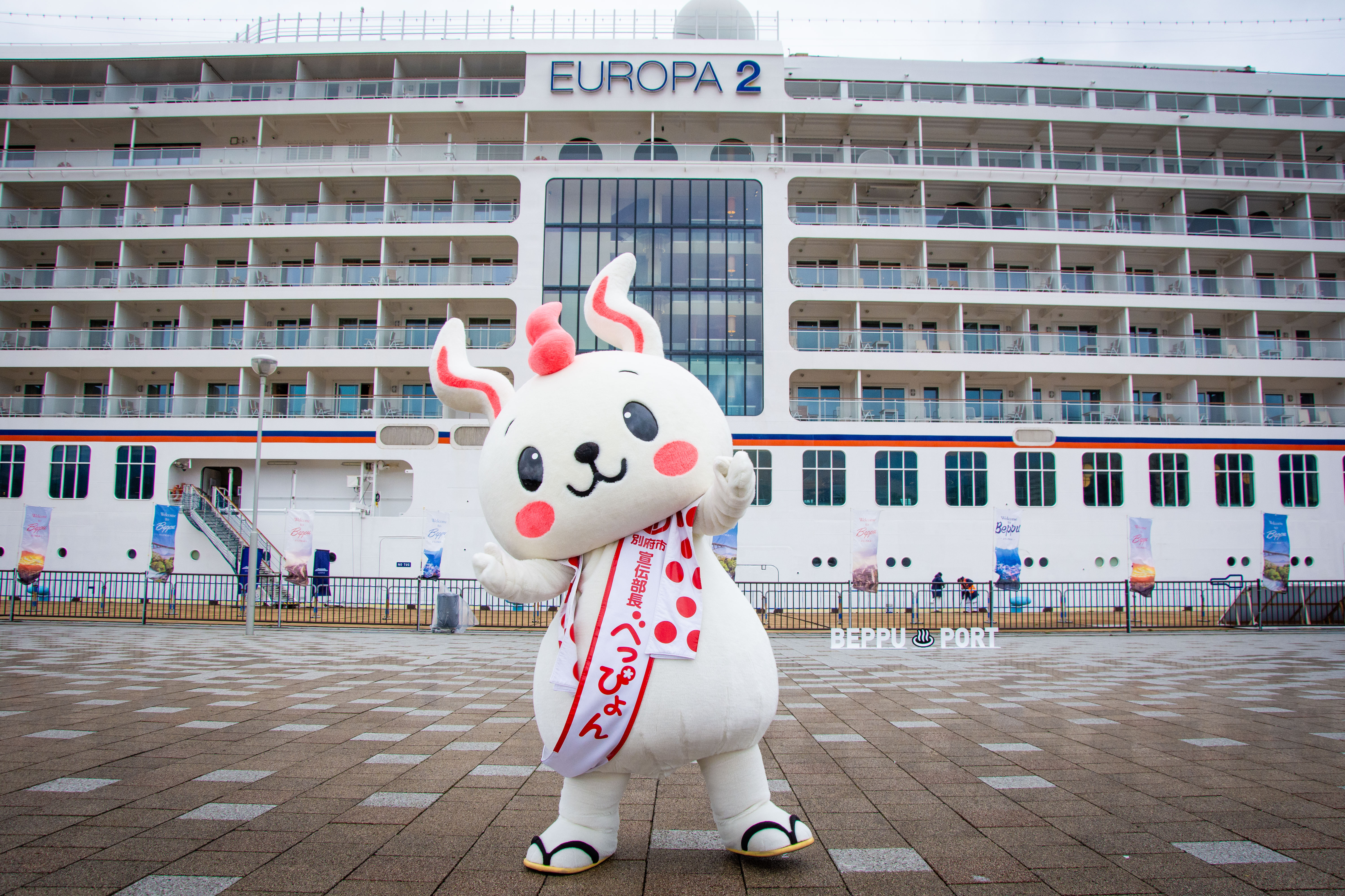 Ein Maskottchen winkt vor der EUROPA 2 in Beppu.